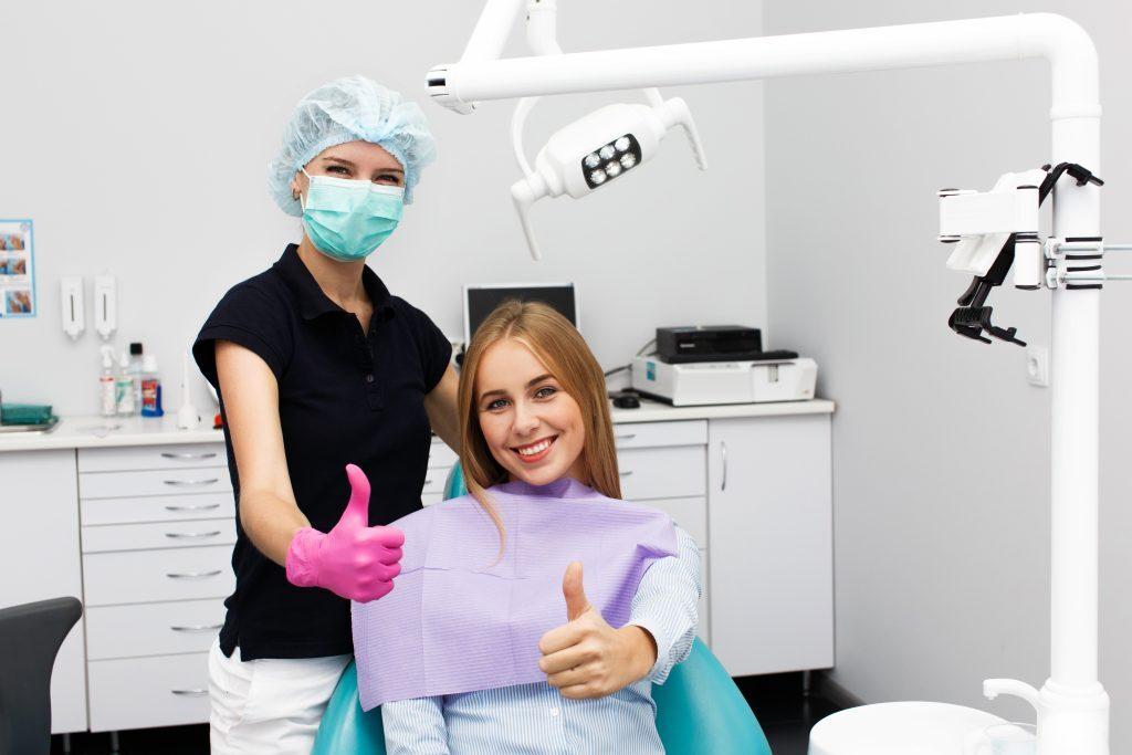 Woman shows thumb up sitting with a stomatologist at dentist off